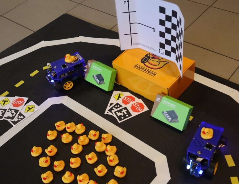 top view of duckiebots on a section of duckietown, rubber duckies scattered around, traffic signs