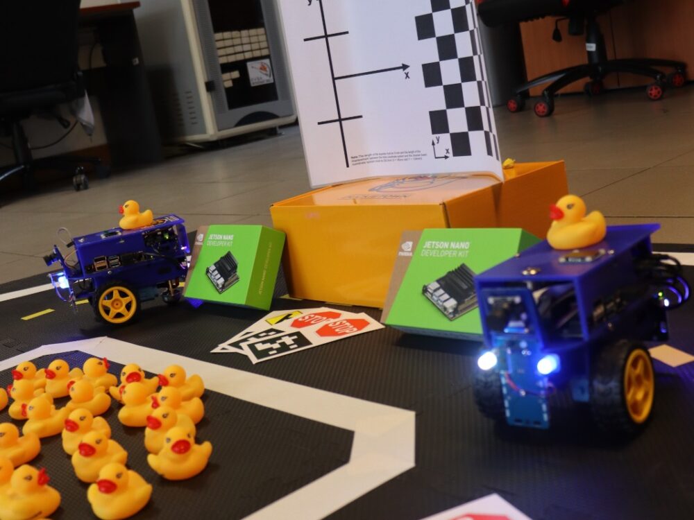 side view of duckiebots on a section of duckietown, rubber duckies scattered around, traffic signs